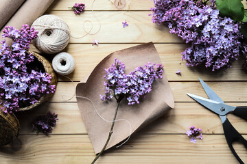 Florist's workshop. Creating a bouquet of lilac. Spring flowers. A sprig of lilac on craft paper. A gift for a girl. Romantic style. Thread, scissors, paper. Wooden table. Handmade work. Hobby