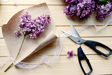 Florist's workshop. Creating a bouquet of lilac. Spring flowers. A sprig of lilac on craft paper. A gift for a girl. Romantic style. Thread, scissors, paper. Wooden table. Handmade work. Hobby