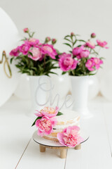 Baby girl one year cake smash peony party. White naked cake with pink peonies on the top. Birthday party decorations