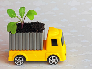 toy truck delivering a container with fertile soil and compost with a green sprout