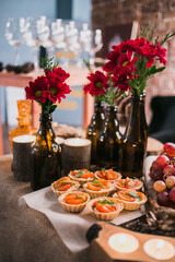 Reserved table with various snacks at the party. Canape with salmon and ruccola, grapes. Decorated with flowers in bottles. Buffet on holiday.