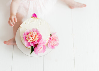 White naked cake with pink peonies on the top. Birthday party decorations. Baby eating the cake top view