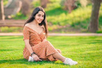 Fototapeta premium beautiful caucasian smiling girl sitting on the grass in the park looking at the camera. great copy space.