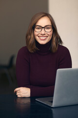 Portrait of beautiful smiling female student wearing glasses, sitting in front of her laptop,...