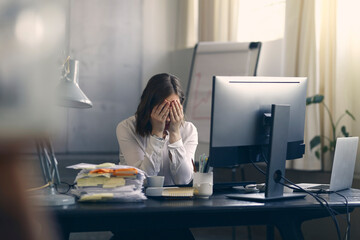 Very stressed business woman sitting in front of her computer with her hands in front of her eyes, feeling sad and depressed