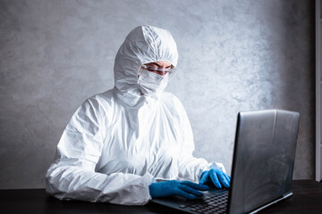 A virologist in a white mask and medical gloves dressed in a white protective suit works with a...