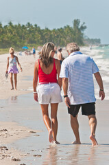 Back view, medium distance of middle aged, couple walking a sandy, tropical, beach, shoreline on gulf of Mexico, on sunny morning