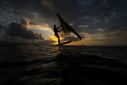 Girl rides a wing foil in the sunset.