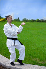 A karate trainer is wearing a white kimono. Black belt in karate. Training in nature. Karate training on a green lawn.