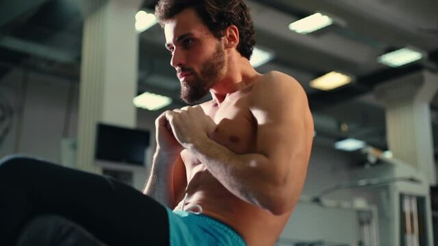 Athletic bearded young man with muscular wiry naked torso doing abdominal crunches during sport workout training in modern gym. Concept of healthy lifestyle. Shooting in slow motion.