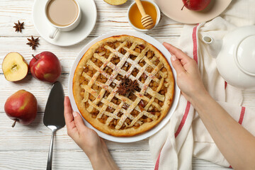 Female hands hold plate with apple pie on white wooden background, top view