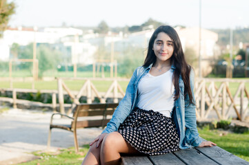 natural beautiful caucasian girl looking at the camera sitting on a wodden bench in the park.