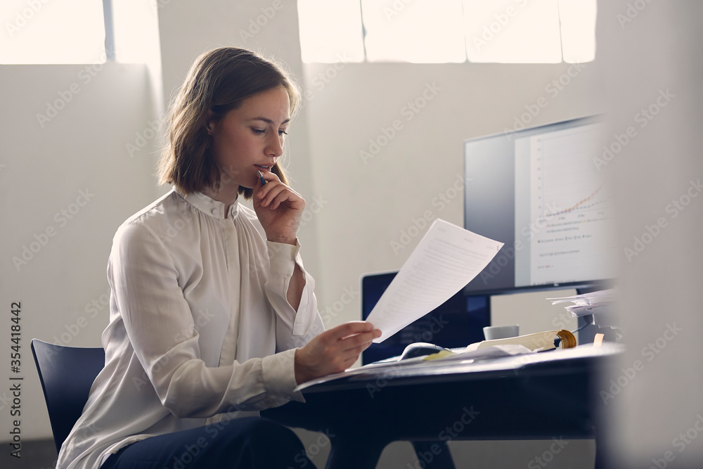 Wall mural pretty female ceo sitting infront of computer while reviewing some paper work