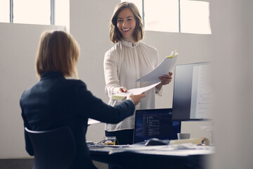 Attractive young and beautiful businesswoman handing over paperwork to her female CEO in the office...