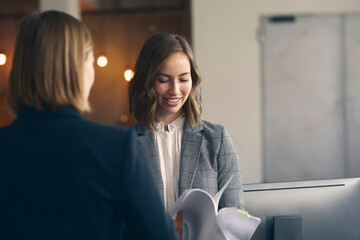 Beautiful young businesswoman and female employee looking at paperwork with female coworker at the office. 
