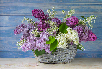A bouquet of multi-colored lilac with lilies of the valley on the background of a blue wall.