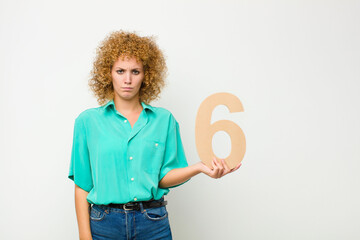 young pretty afro woman sad, depressed, unhappy, holding a number 6.