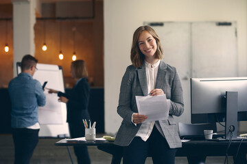 Portrait of happy businesswoman signing of som paperwork while standing infront of her desk and her...