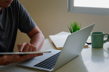 An Asian man uses a laptop at home while sitting at a wooden table. Man hands typing on a notebook keyboard.