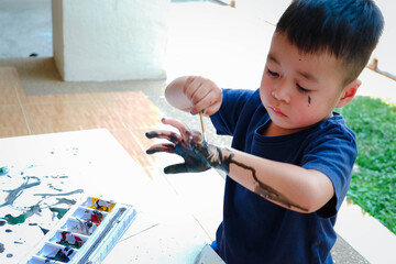 Asian little boy with hand painted in colorful paints, workshop for children concept. Leaning and education of kid at home.