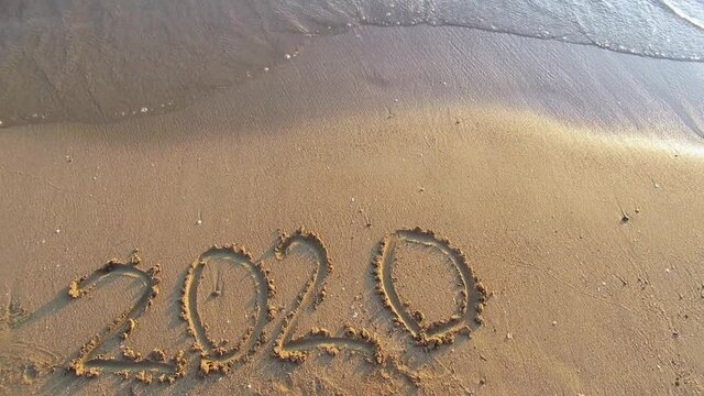 Title 2020 on sandy beach with a sea waves above. Sea surf.