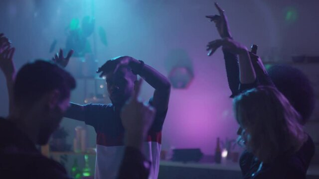  Handheld slowmo of group of young friends dancing with their arms raised at house party