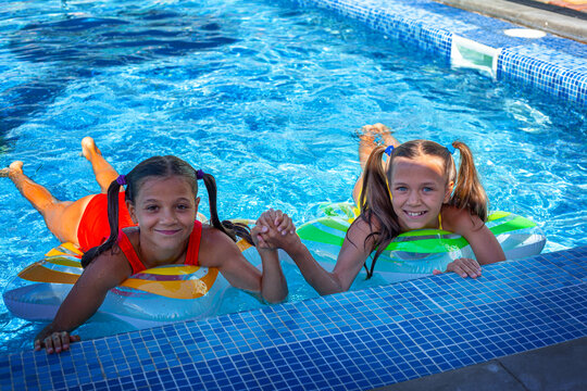 Two tween girls playing, splashing, laughing and have fun in the blue water of swimming pool with inflatanle rings.