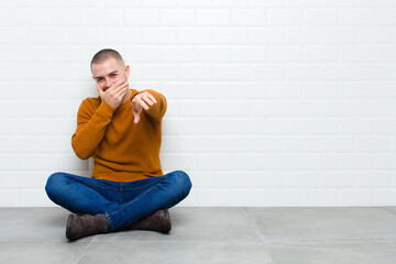 young handsome man laughing at you, pointing to camera and making fun of or mocking you sitting on...