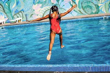 Back view of the preteen girl jumping to dive in the blue water of the pool