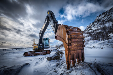 Old excavator with excavator bucket in winter. Road construction in snow. Lofoten islands, Norway....
