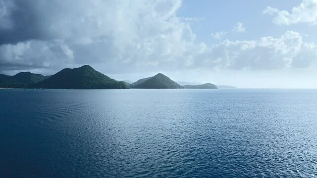 Drone camera approaches the mountains on the shore through the blue sea, yachts sail nearby (Saint Lucia)
