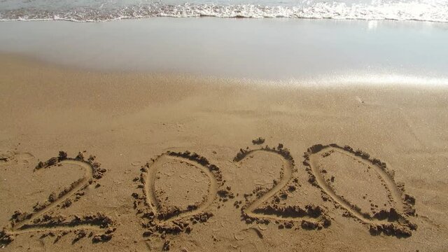 Title 2020 on sandy beach with a sea waves above. Sea surf.