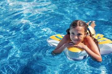 Preteen girl dressed red  swimsuit swimming in the blue resort pool on the inflatanle ring. Summer...