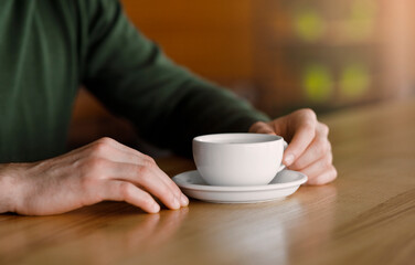 Man hands holding cup of coffee, cafe interior