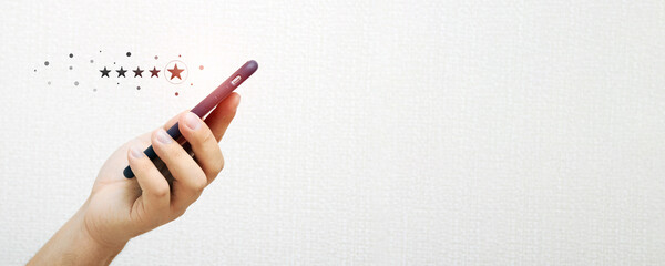 Close up of a person's hand holding a smartphone with an icon of a five star rating feedback on the...