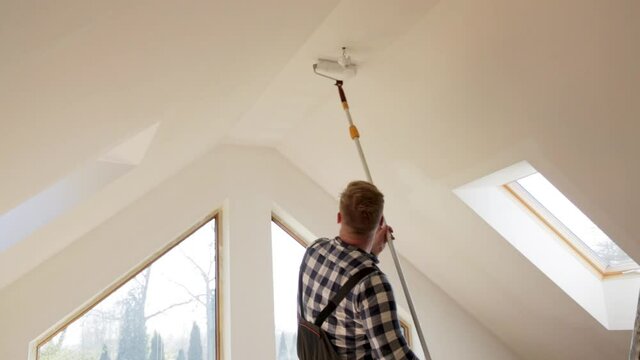 Home improvement concept, handyman painting a wall with a white paint near roof window in attic