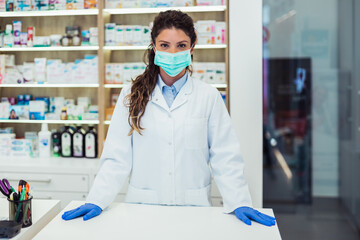 Female pharmacist with protective mask on her face working at pharmacy. Medical healthcare concept.