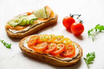 Variety of sandwiches for breakfast, snack, appetizers - tomatoes, bacon, cucumbers, cream cheese, whole grain bread sandwiches. On a light background.