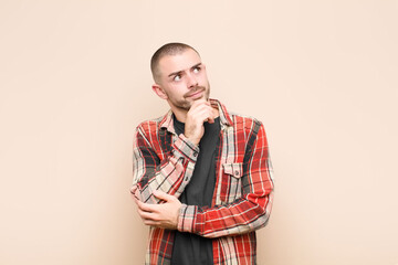young handsome man thinking, feeling doubtful and confused, with different options, wondering which...