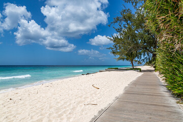 Looking along a wooden boardwalk running alongside a sandy Caribbean beach
