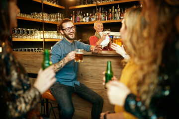 Group of cheerful friends standing near bar counter, drinking beer and chatting.