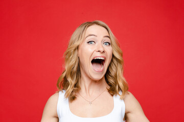 Young beautiful caucasian woman with medium fair wavy hair and nude makeup in white t-shirt rejoices, picture isolated on red background