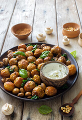 Fried little potatoes and mushrooms on clay plate on natural wooden background