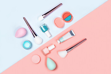 Makeup products with brushes, nail polish, sponges, eyeshadow, cream and lipstick on coral-blue color background. Flat lay, top view, space for text.