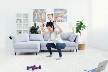 Beautiful mommy and charming little daughter are smiling while doing fitness exercises together at home.