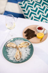 fresh seafood. Oysters lie on a plate with ice. In the background is a glass of white wine. A plate with sauce and vinegar and black croutons. White tablecloth. A restaurant. Blue pillows
