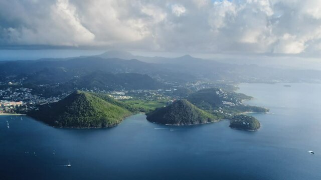 Drone view of two mountains on the shore, yachts sail in the sea, on the horizon an island with a city, cloudy (Saint Lucia)