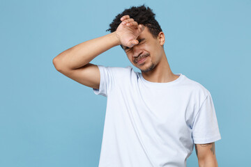 Fototapeta premium Exhausted tired young african american guy in casual white t-shirt posing isolated on pastel blue background studio. People lifestyle concept. Mock up copy space. Put hand on head keeping eyes closed.