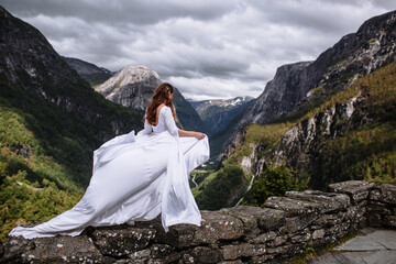 A bride walking along the edge of a stone wall against a beautiful mountain landscape