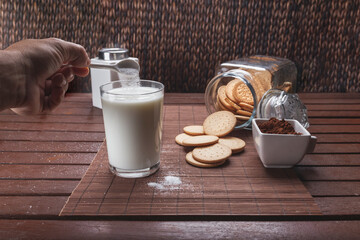 still life of cookies milk azurac cocoa, in rustic brown colors putting sugar in glass of milk